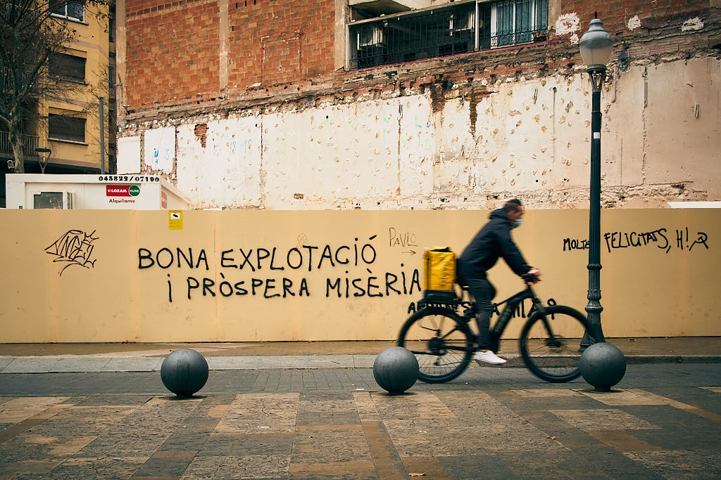 Un rider de Glovo circula per davant d'una pintada en l'avinguda de Gaudí de Barcelona en ple debat sobre la Llei Rider.