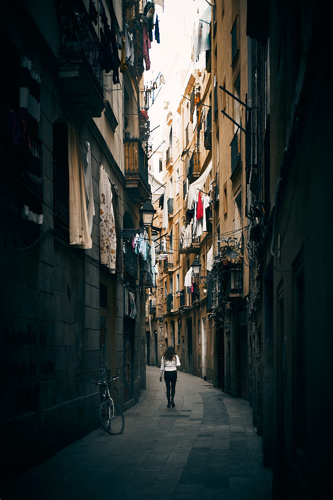 Una noia es passeja pel carrer dels Cecs de Sant Cugat, en el barri de la Ribera de Barcelona, sota balcons atapeïts de roba estesa.