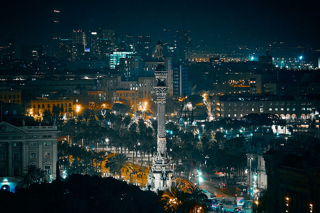 Panoràmica nocturna de Ciutat Vella amb el monument de Cristòfor Colom i el Port Vell de Barcelona en primer terme i les tres xemeneies de Sant Adrià de Besòs al fons.