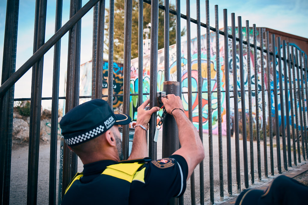 A Municipal Police agent locks with key the padlock which secures the bars of the north access to the Bunkers del Carmel for the third day in a row